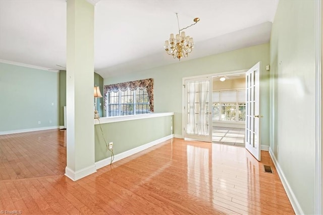 spare room featuring wood-type flooring, an inviting chandelier, and french doors