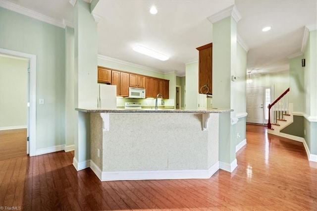 kitchen with a breakfast bar, hardwood / wood-style floors, white appliances, crown molding, and kitchen peninsula