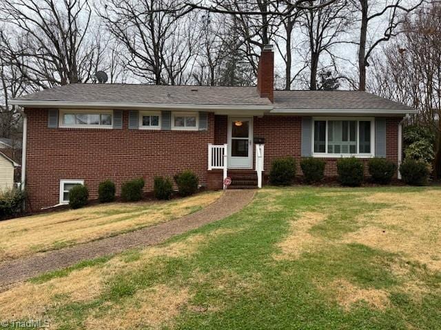 single story home with brick siding, a chimney, and a front yard