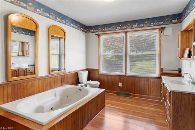 bathroom featuring toilet, a bathtub, hardwood / wood-style floors, vanity, and wood walls