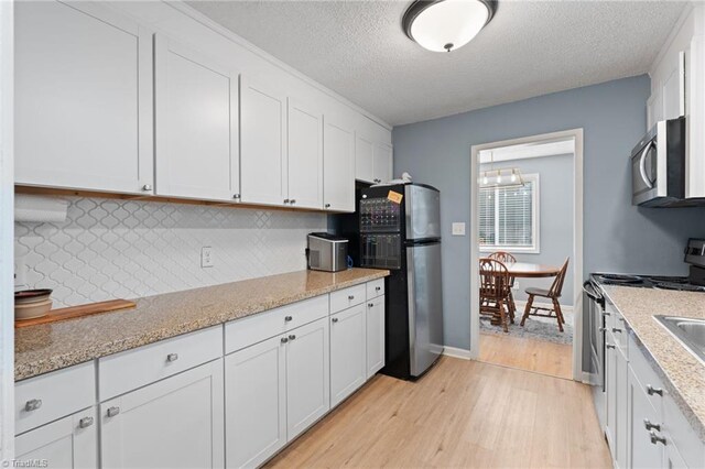 kitchen featuring white cabinets, a textured ceiling, stainless steel appliances, and light stone counters