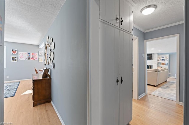 hallway featuring light hardwood / wood-style floors, a textured ceiling, and ornamental molding