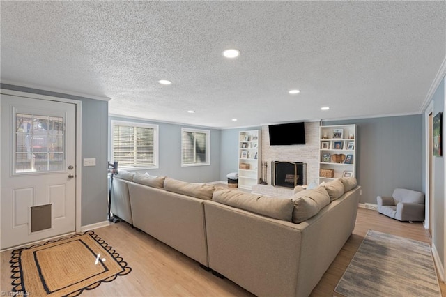 living room with light hardwood / wood-style flooring, a brick fireplace, built in shelves, ornamental molding, and a textured ceiling