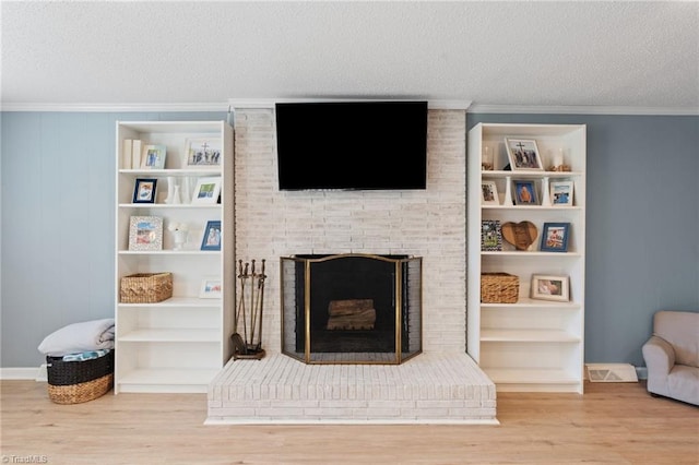 living room with hardwood / wood-style floors, ornamental molding, a textured ceiling, and a brick fireplace