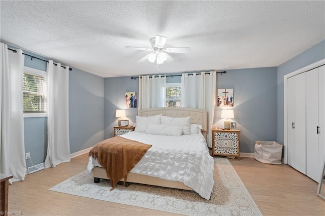 bedroom featuring a textured ceiling, a closet, light hardwood / wood-style flooring, and ceiling fan