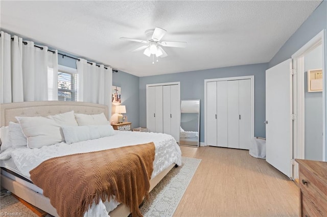 bedroom featuring a textured ceiling, ceiling fan, light hardwood / wood-style flooring, and multiple closets