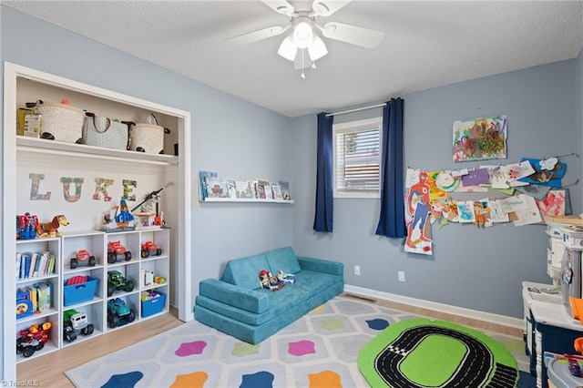 rec room with ceiling fan, light hardwood / wood-style floors, and a textured ceiling