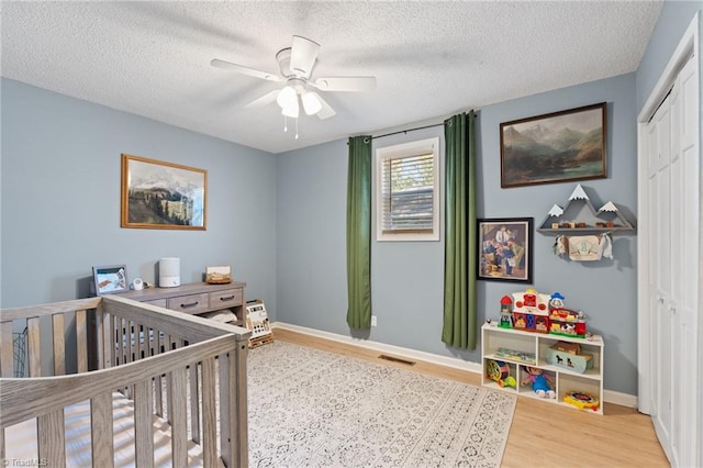 bedroom featuring a textured ceiling, ceiling fan, a crib, light hardwood / wood-style floors, and a closet