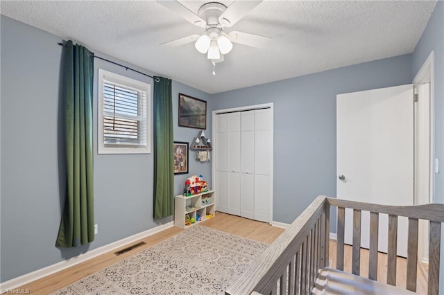 bedroom with ceiling fan, light wood-type flooring, a textured ceiling, a crib, and a closet