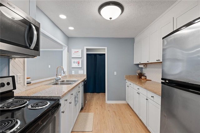 kitchen with sink, light wood-type flooring, light stone countertops, appliances with stainless steel finishes, and white cabinetry