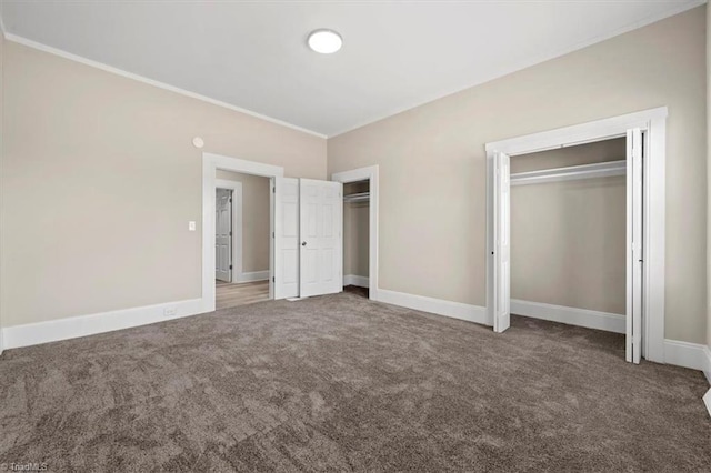 unfurnished bedroom featuring baseboards, ornamental molding, two closets, and carpet flooring