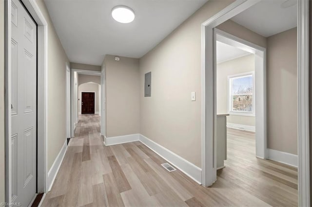 hallway featuring arched walkways, light wood finished floors, visible vents, and baseboards