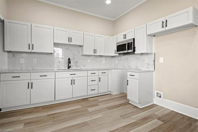 kitchen with a sink, white cabinets, light wood-style floors, backsplash, and stainless steel microwave