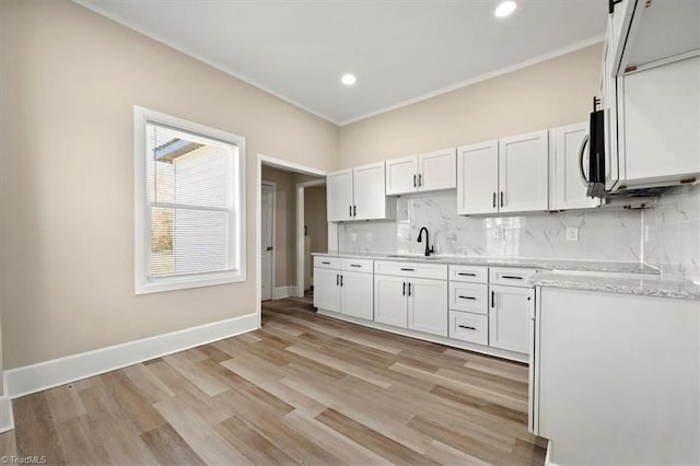 kitchen featuring tasteful backsplash, baseboards, white cabinets, and a sink