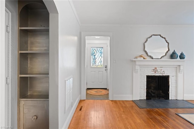 interior space with ornamental molding, built in features, wood-type flooring, and a brick fireplace