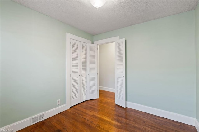 unfurnished bedroom featuring a textured ceiling, dark hardwood / wood-style flooring, and a closet