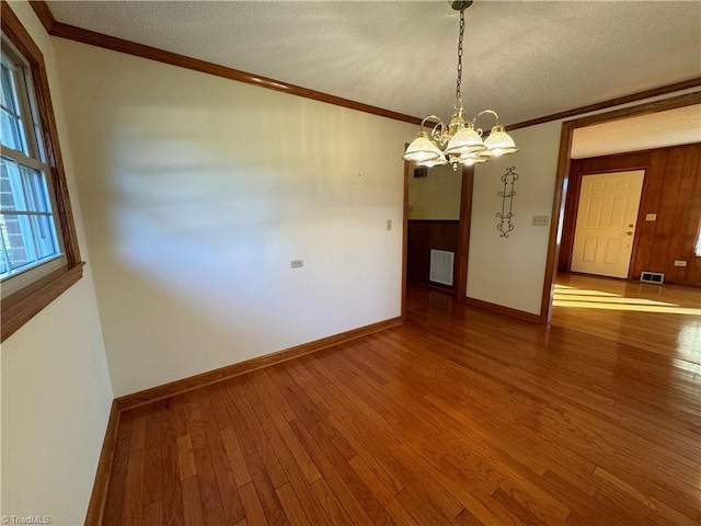 unfurnished dining area with a textured ceiling, wood-type flooring, ornamental molding, and a chandelier