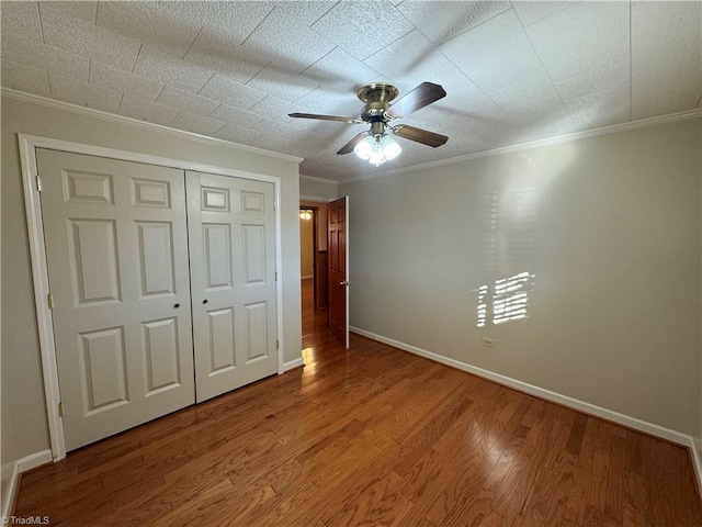 unfurnished bedroom featuring crown molding, hardwood / wood-style floors, ceiling fan, and a closet