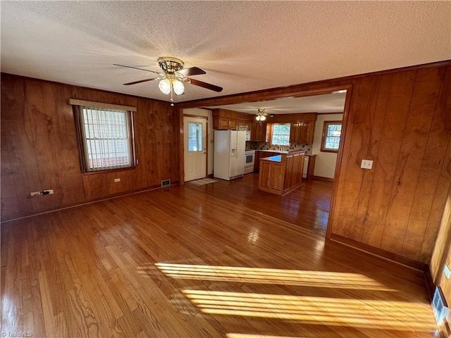 interior space featuring ceiling fan, light hardwood / wood-style floors, a textured ceiling, and wood walls