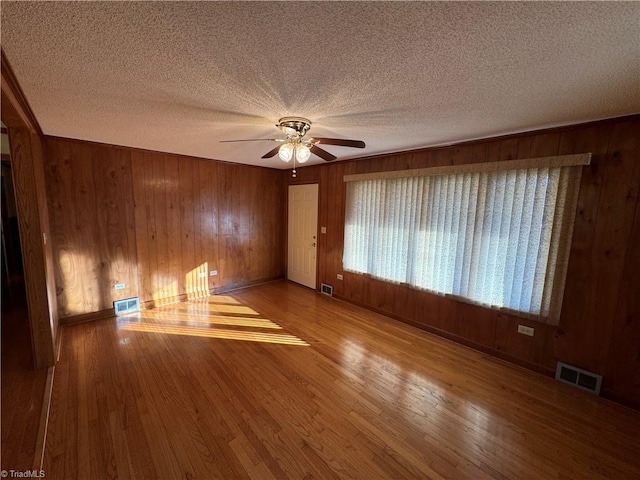 empty room featuring hardwood / wood-style flooring, wooden walls, a textured ceiling, and ceiling fan