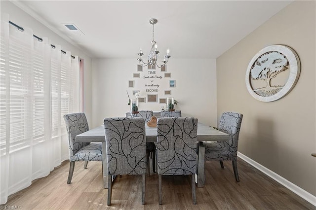 dining room with a chandelier, baseboards, visible vents, and wood finished floors