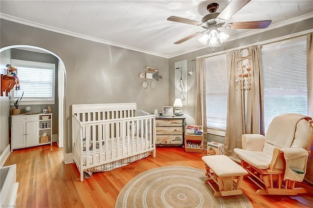 bedroom with ceiling fan, crown molding, a crib, and light wood-type flooring