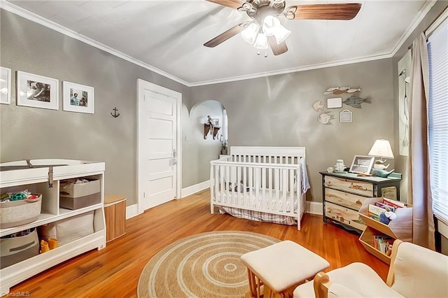 bedroom with hardwood / wood-style floors, ceiling fan, crown molding, and a nursery area