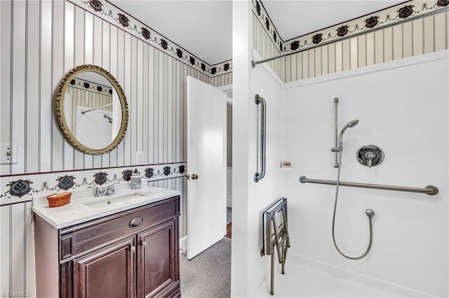 bathroom featuring walk in shower, vanity, and wallpapered walls