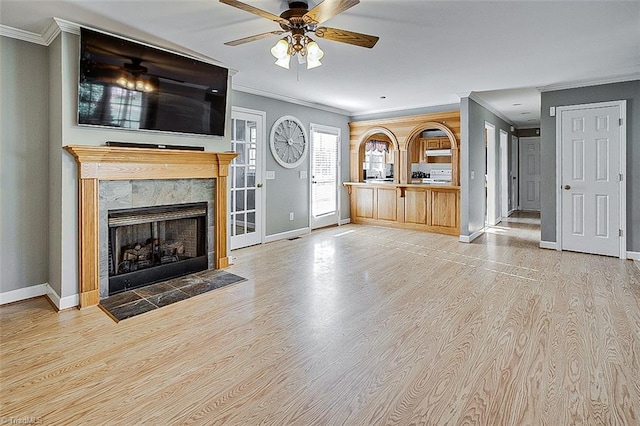 unfurnished living room featuring crown molding, a tile fireplace, light wood-type flooring, and ceiling fan