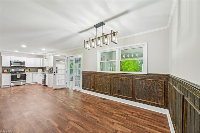kitchen with appliances with stainless steel finishes, crown molding, white cabinets, wood finished floors, and pendant lighting