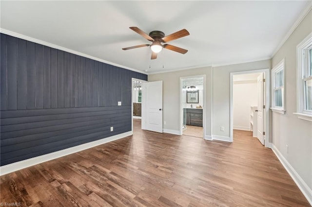 unfurnished bedroom with crown molding, wood finished floors, a spacious closet, baseboards, and connected bathroom