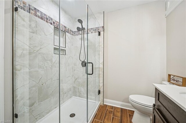 bathroom with wood tiled floors, a shower stall, toilet, vanity, and baseboards