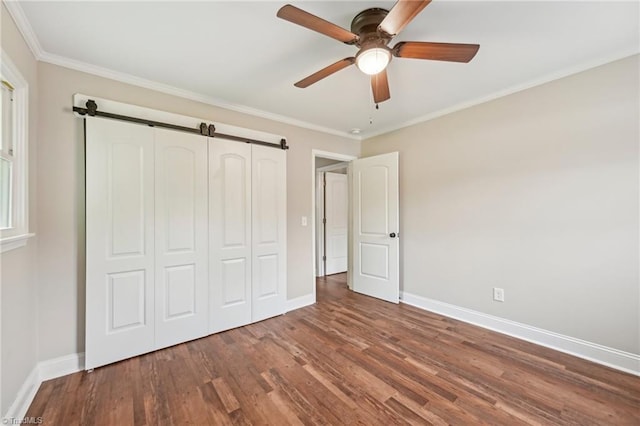 unfurnished bedroom featuring baseboards, wood finished floors, a barn door, a closet, and crown molding