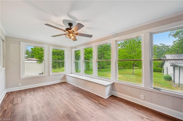 unfurnished sunroom featuring baseboards, wood finished floors, and crown molding