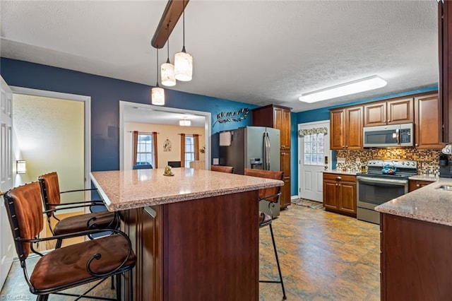 kitchen with backsplash, a center island, light stone countertops, a breakfast bar area, and appliances with stainless steel finishes