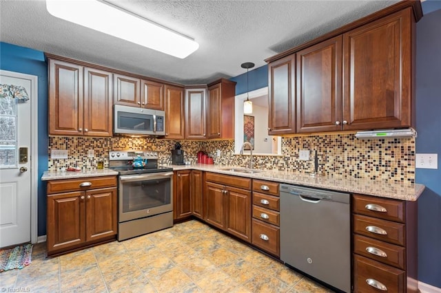 kitchen with brown cabinetry, a sink, appliances with stainless steel finishes, decorative light fixtures, and backsplash