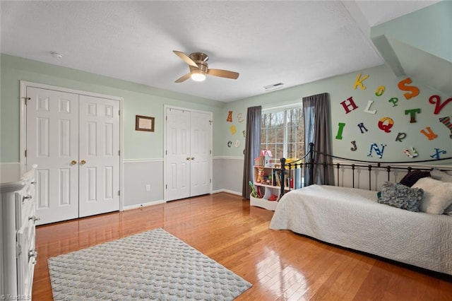 bedroom with wood finished floors, baseboards, ceiling fan, a textured ceiling, and two closets