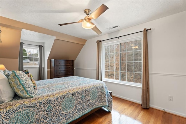 bedroom with a ceiling fan, baseboards, wood finished floors, visible vents, and a textured ceiling