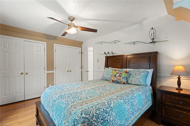 bedroom featuring light wood finished floors, ceiling fan, a textured ceiling, and multiple closets