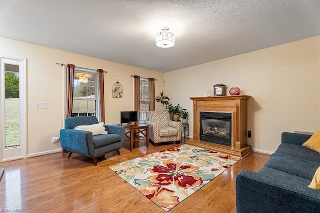 living room featuring a glass covered fireplace, wood finished floors, baseboards, and a textured ceiling