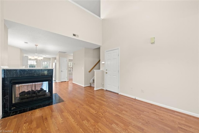 unfurnished living room with an inviting chandelier, a multi sided fireplace, hardwood / wood-style flooring, and a towering ceiling