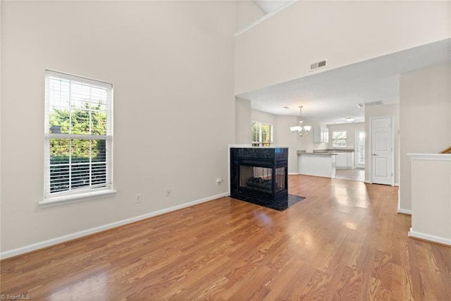 unfurnished living room with an inviting chandelier, a multi sided fireplace, light hardwood / wood-style flooring, and a towering ceiling