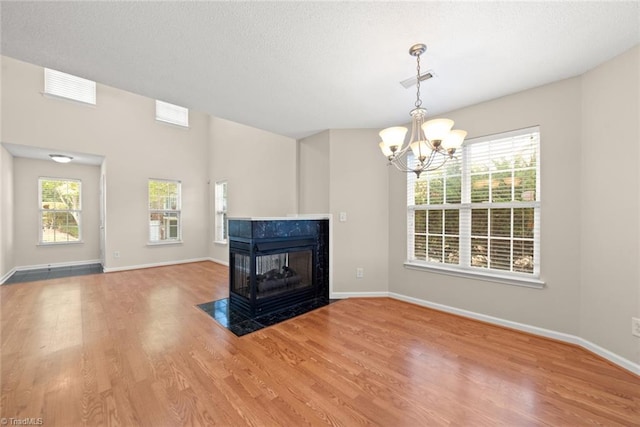 unfurnished living room featuring a multi sided fireplace, hardwood / wood-style flooring, and a notable chandelier