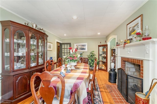 dining area with light wood-type flooring, crown molding, and a brick fireplace