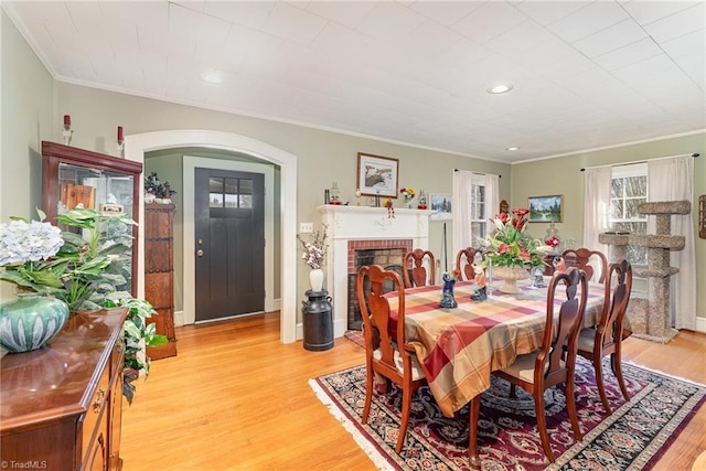 dining room with a fireplace, light wood-type flooring, and crown molding