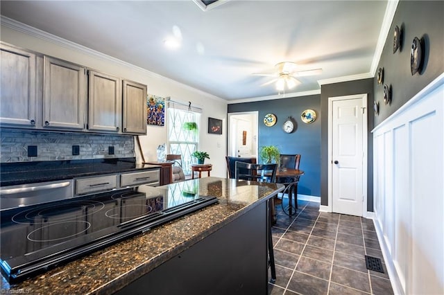 kitchen with crown molding, dark tile patterned floors, ceiling fan, backsplash, and dark stone counters