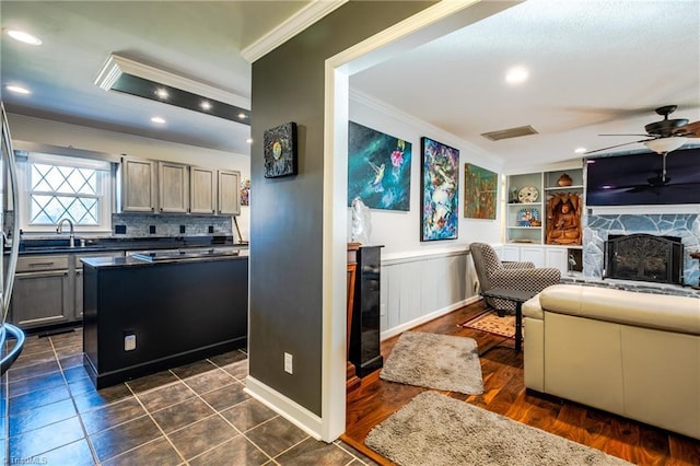 interior space with a kitchen island, a fireplace, gray cabinetry, ornamental molding, and ceiling fan