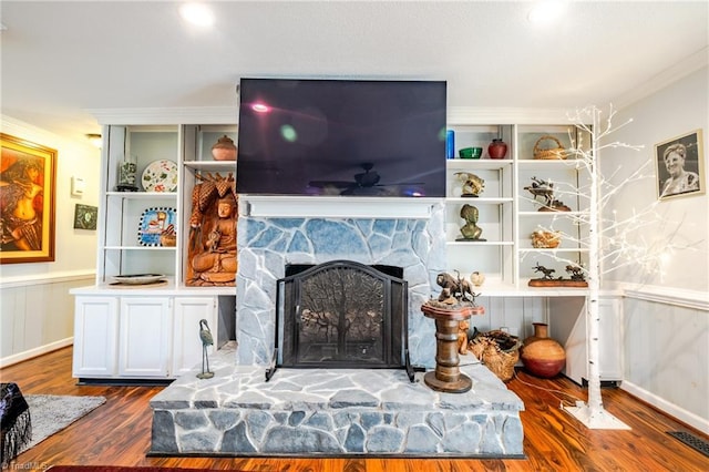 living room with dark hardwood / wood-style flooring, a stone fireplace, crown molding, and built in shelves