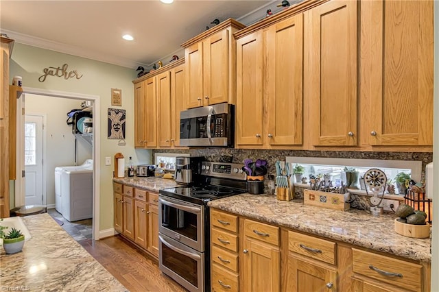 kitchen featuring ornamental molding, wood finished floors, stainless steel appliances, washer and dryer, and backsplash