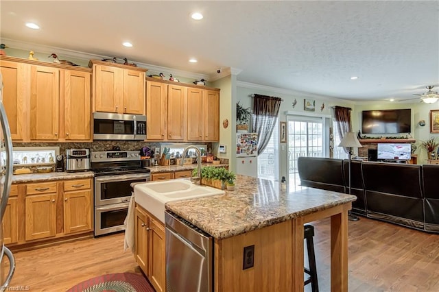 kitchen with a breakfast bar area, stainless steel appliances, light wood-style flooring, open floor plan, and a sink